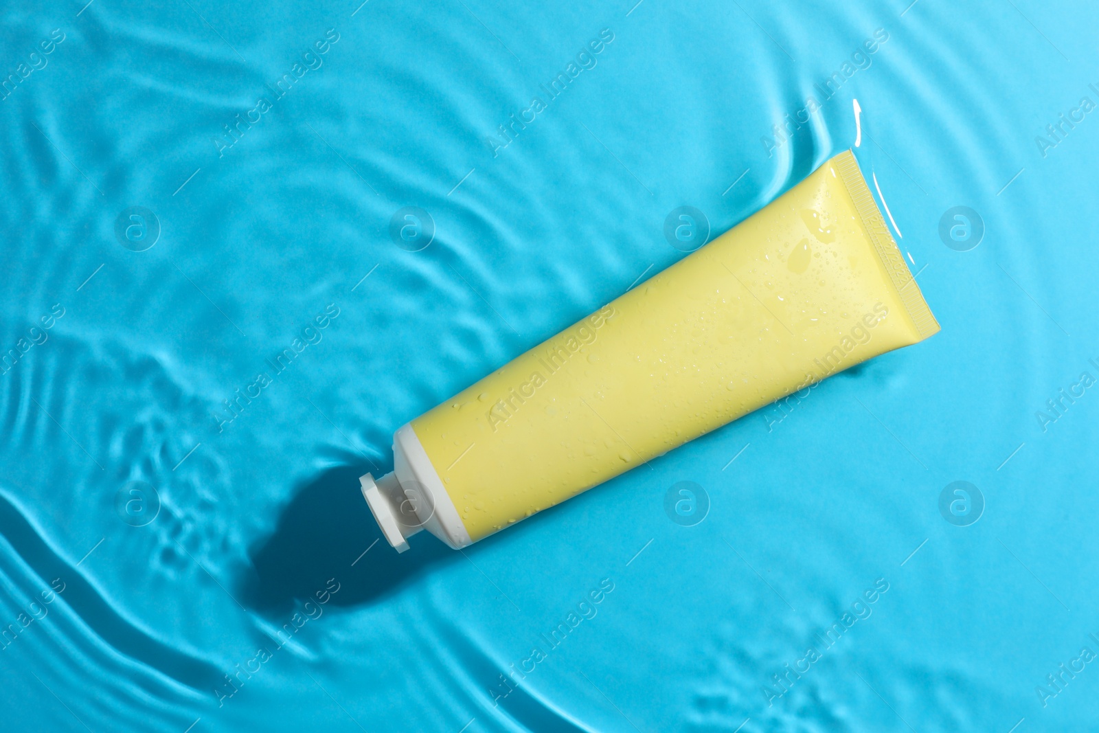 Photo of Tube with moisturizing cream in water on light blue background, top view