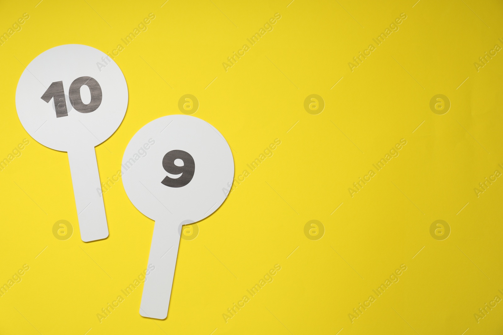 Photo of Auction paddles with numbers on yellow background, flat lay. Space for text