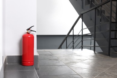 Red fire extinguisher near white wall, space for text