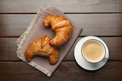 Delicious fresh croissants and cup of coffee on wooden table, flat lay