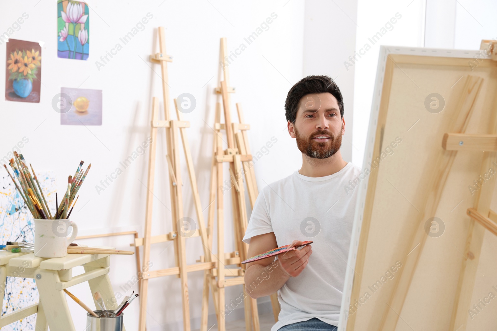 Photo of Man painting in studio. Using easel to hold canvas