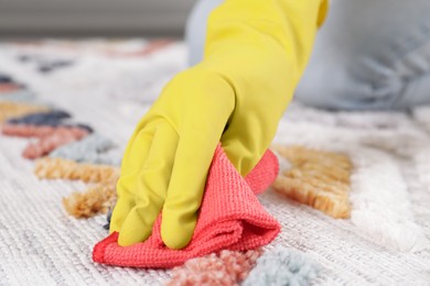 Photo of Woman in rubber gloves cleaning carpet with rag indoors, closeup