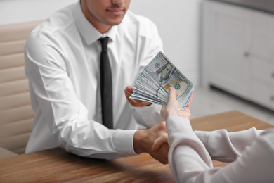 Photo of Woman shaking hands with man and offering bribe at table indoors, closeup