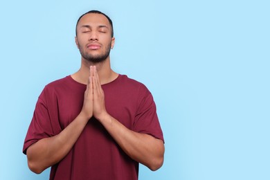 Photo of African American man with clasped hands praying to God on light blue background. Space for text