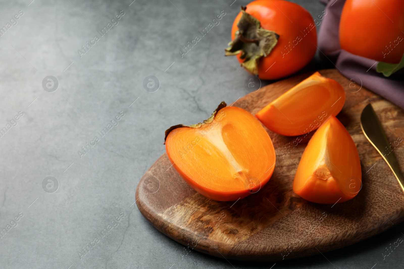 Photo of Delicious ripe persimmons and knife on light gray textured table, space for text