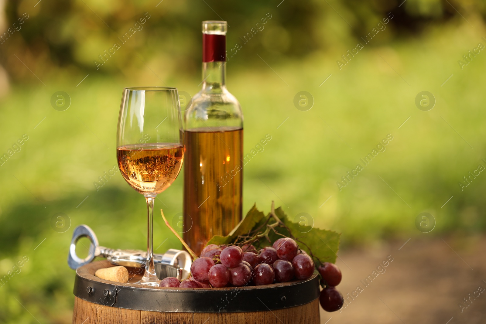 Photo of Delicious wine and ripe grapes on wooden barrel outdoors, space for text