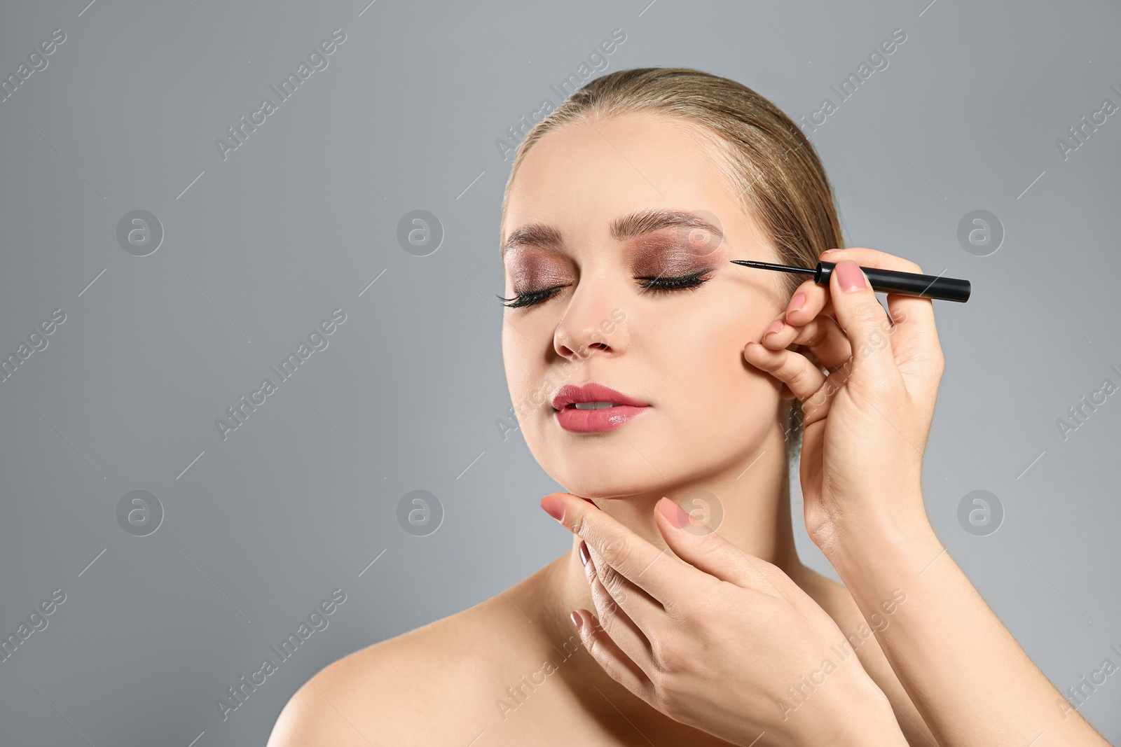 Photo of Artist applying makeup onto woman's face on light grey background