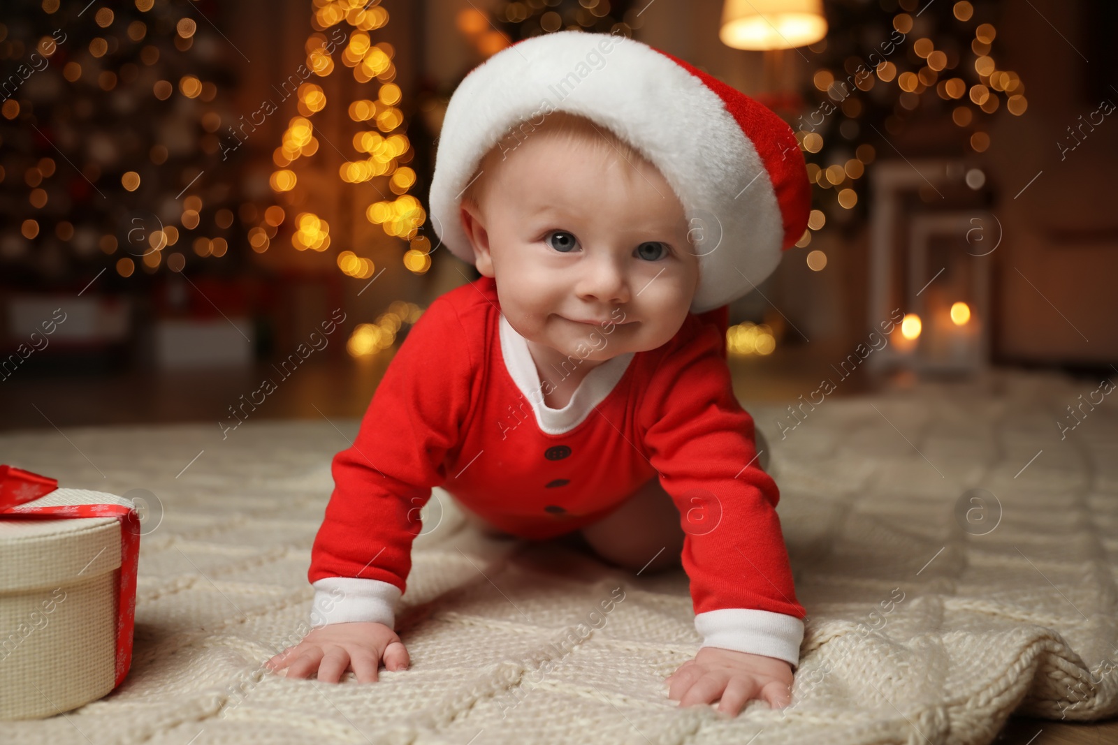 Photo of Cute baby in Santa hat with Christmas gift on floor at home