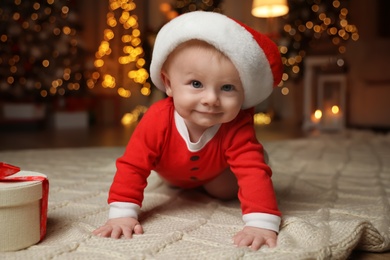 Cute baby in Santa hat with Christmas gift on floor at home