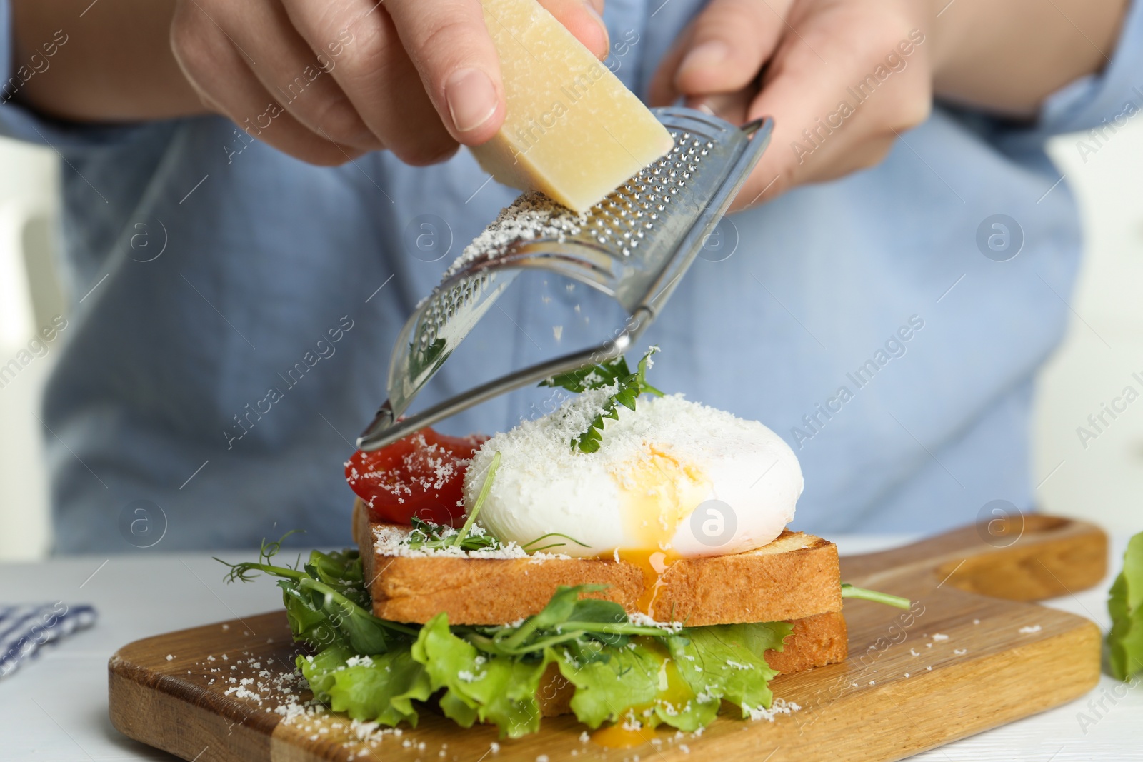 Photo of Woman grating cheese onto poached egg sandwich at table, closeup