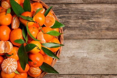 Photo of Fresh ripe juicy tangerines and green leaves on wooden table, top view. Space for text