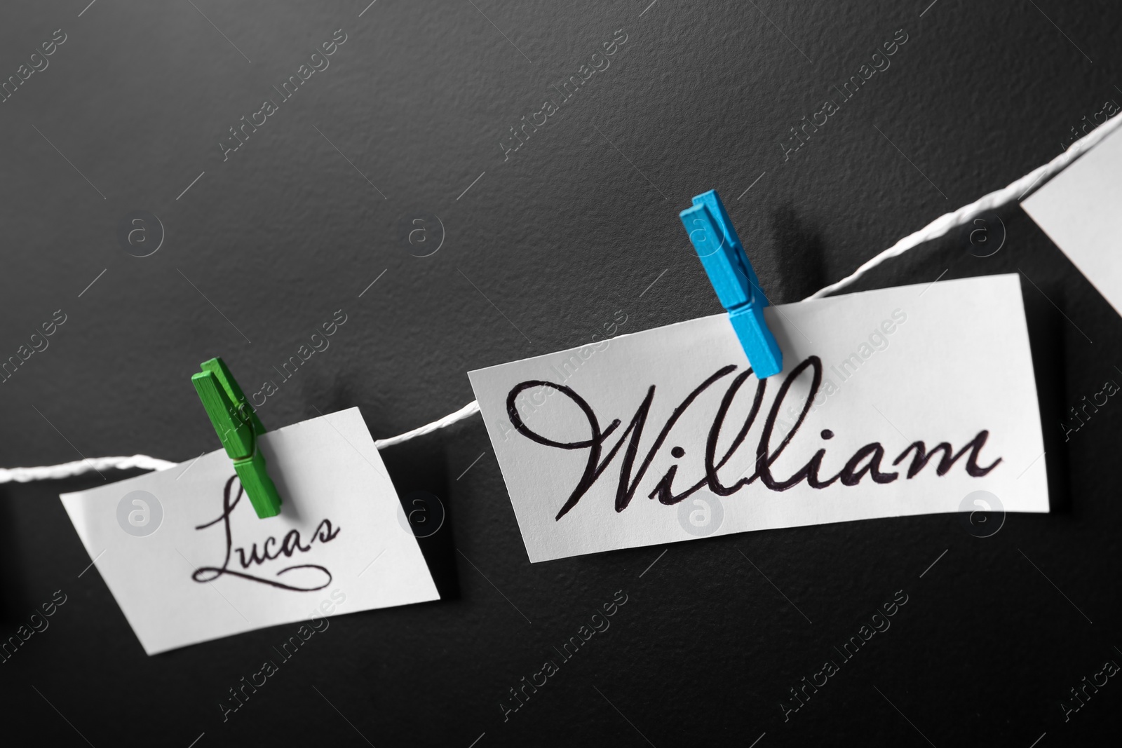 Photo of Paper pieces with baby names on rope against black background, closeup