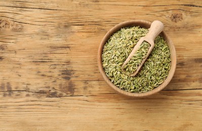 Bowl and scoop with fennel seeds on wooden table, top view. Space for text