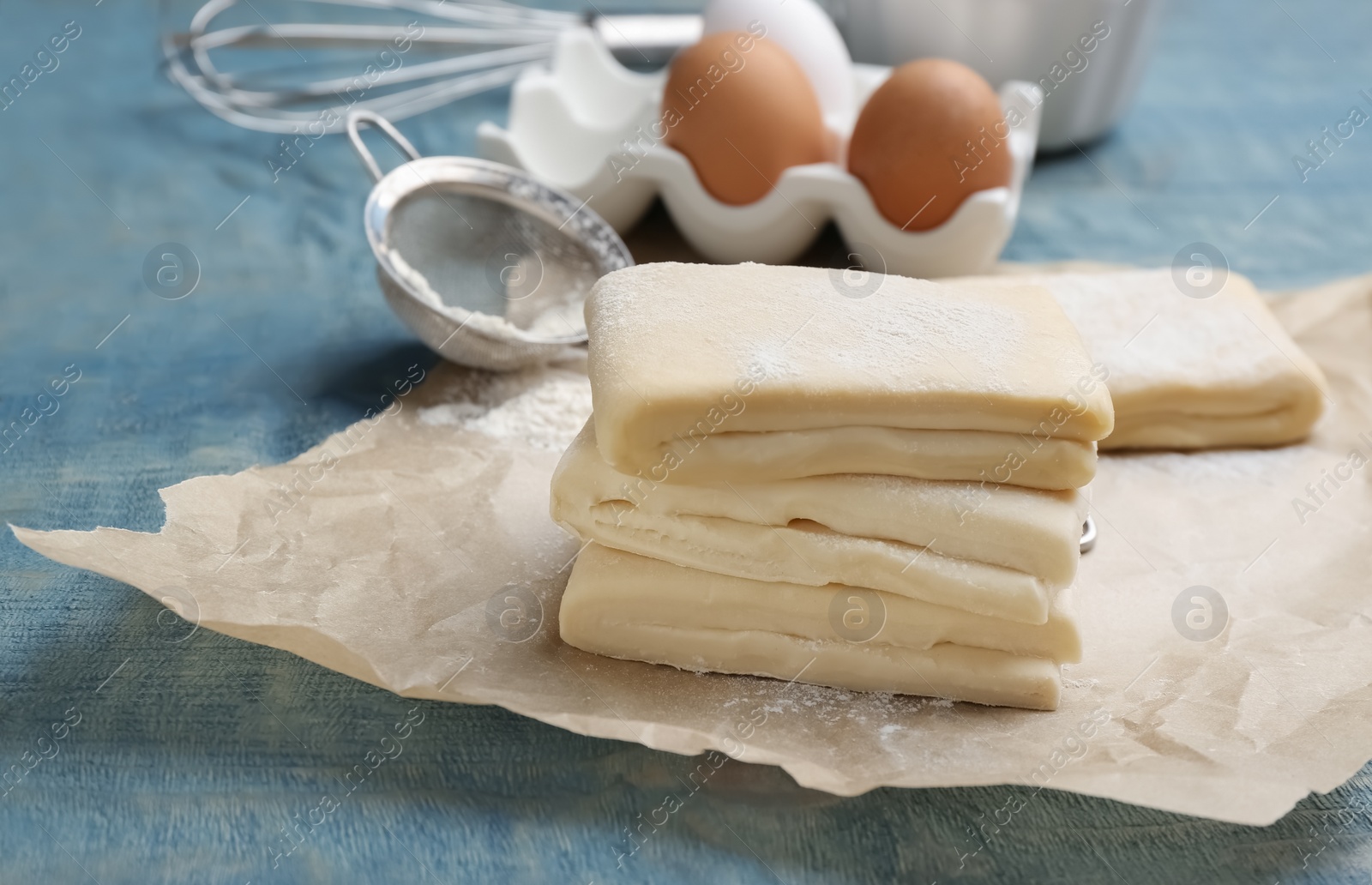 Photo of Parchment with raw wheat dough on table