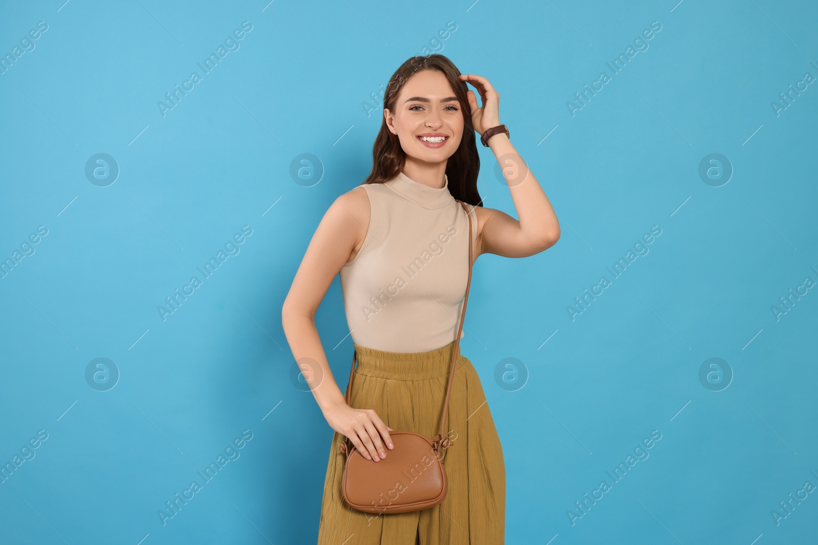 Photo of Beautiful young woman in fashionable outfit with stylish bag on light blue background