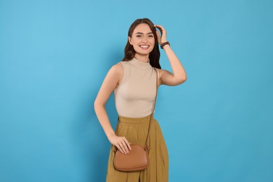 Photo of Beautiful young woman in fashionable outfit with stylish bag on light blue background