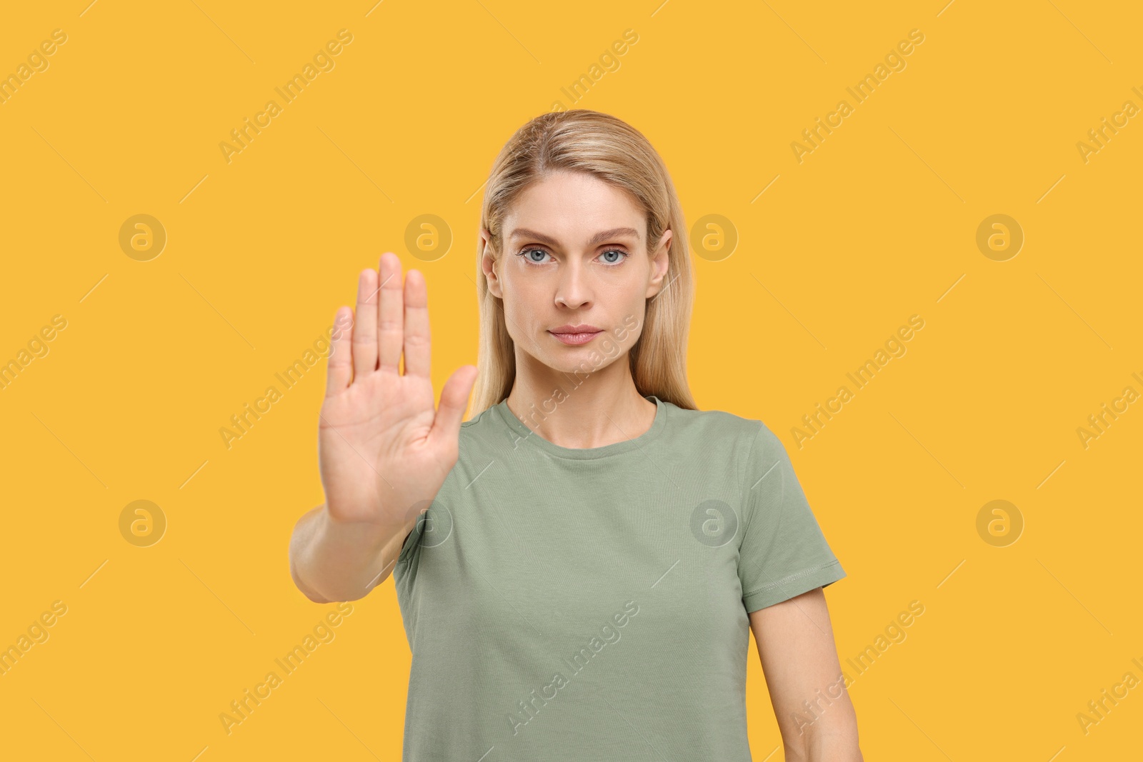 Photo of Woman showing stop gesture on yellow background