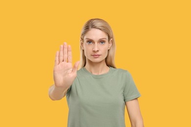 Woman showing stop gesture on yellow background
