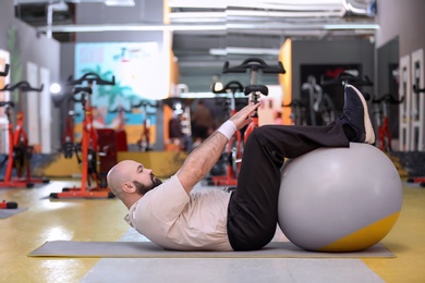 Photo of Overweight man training with fitball in gym