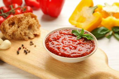 Photo of Delicious adjika sauce in bowl with bread and ingredients on wooden table