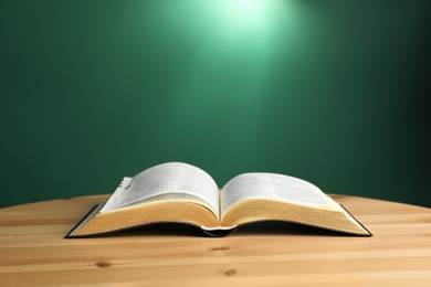 Open Bible on wooden table against green background