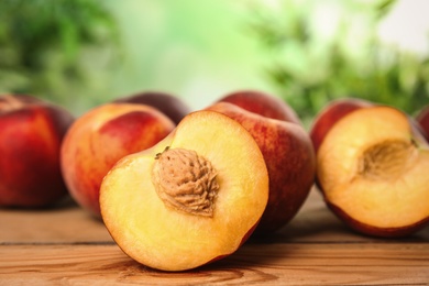 Fresh juicy peaches on wooden table against green blurred background