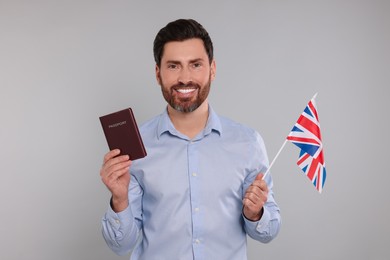 Photo of Immigration. Happy man with passport and flag of United Kingdom on gray background