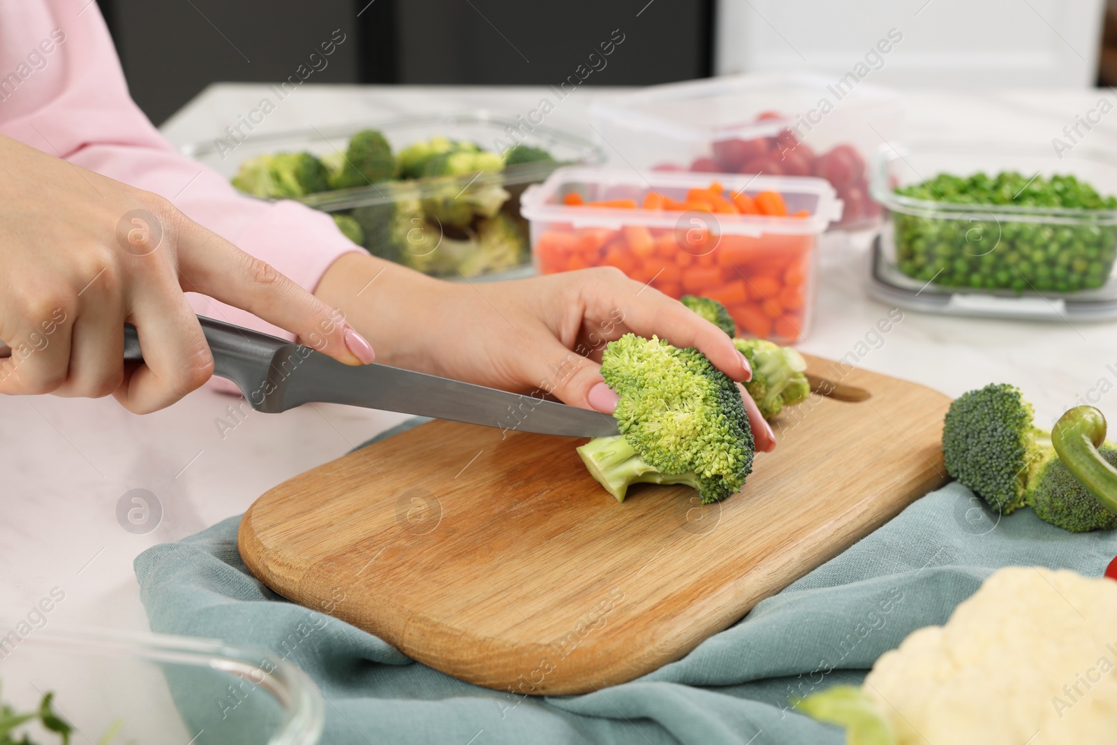 Photo of Woman cutting green broccoli near containers with fresh products at white marble table, closeup