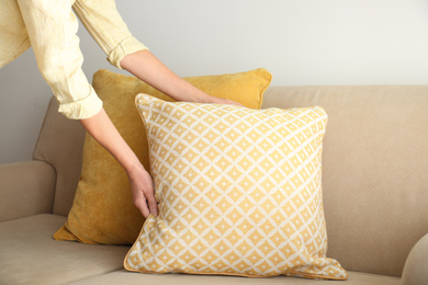 Woman putting pillow onto sofa, closeup view. Interior design