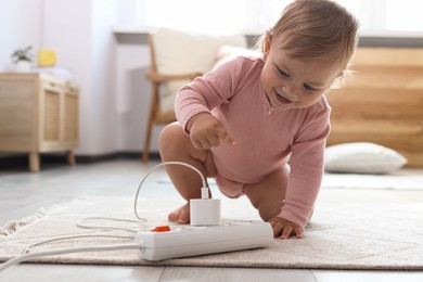 Photo of Cute baby playing with power strip on floor at home. Dangerous situation