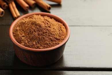 Photo of Bowl of cinnamon powder and sticks on wooden table, closeup. Space for text