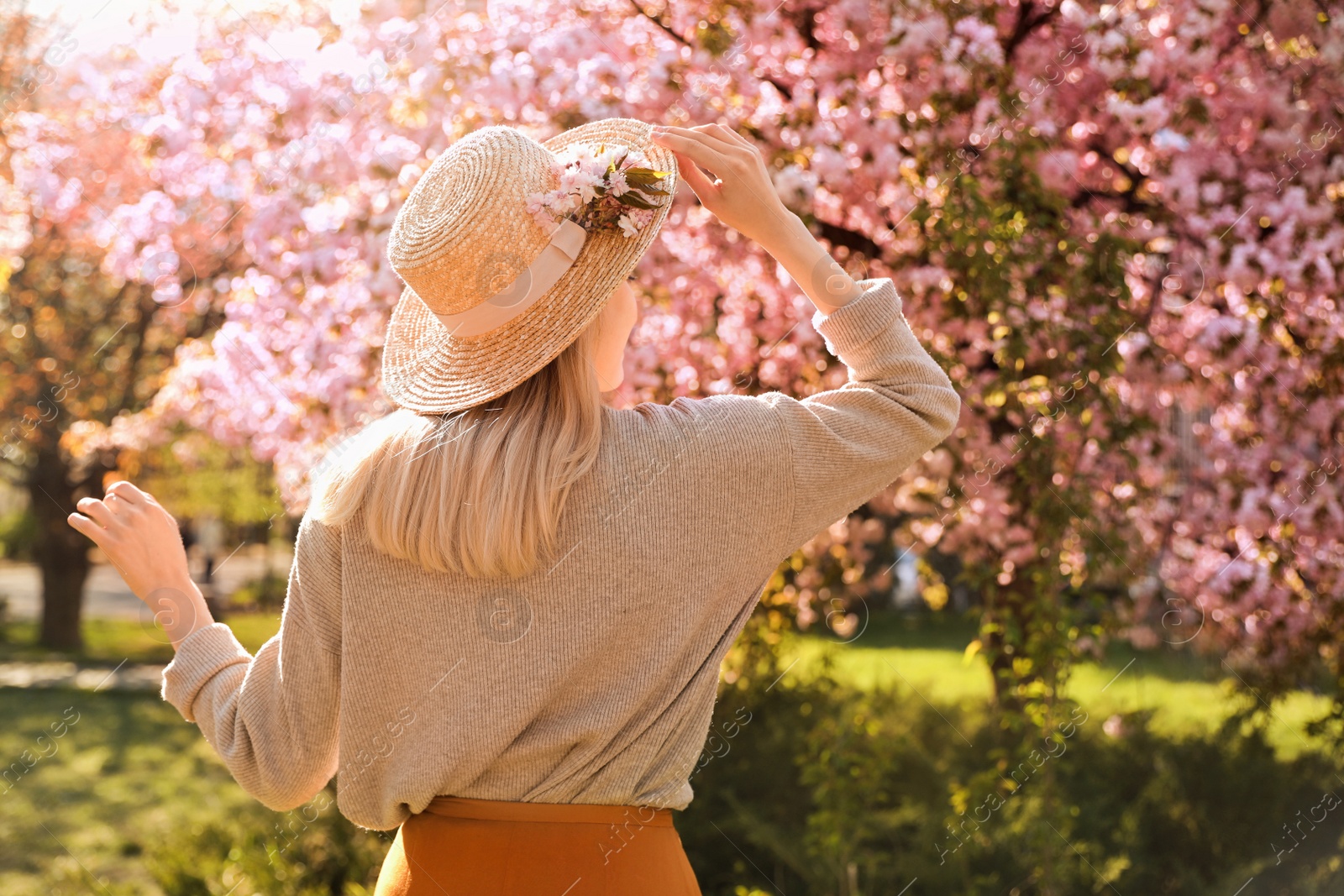 Photo of Young woman wearing stylish outfit in park on spring day, back view. Fashionable look