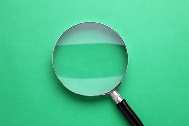 Magnifying glass on green background, top view