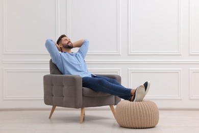 Photo of Handsome man relaxing in armchair near white wall indoors