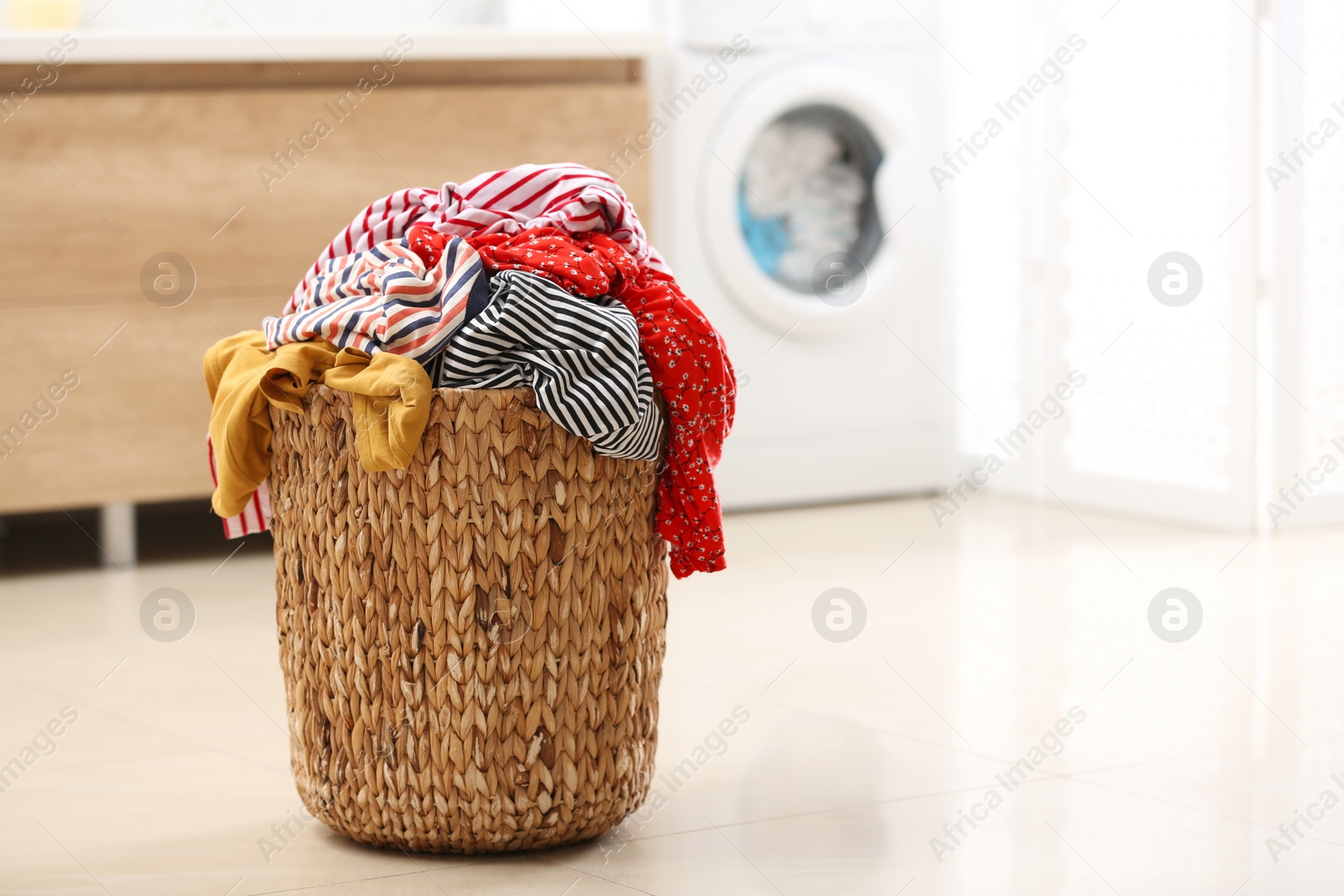 Photo of Wicker basket with dirty clothes on floor in bathroom. Space for text