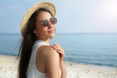 Photo of Beautiful young woman with straw hat and sunglasses on beach. Stylish headdress