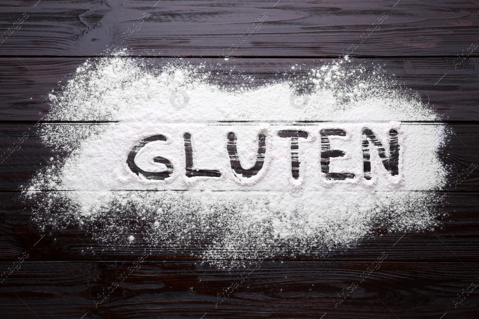 Photo of Word Gluten written with flour on brown wooden table, top view