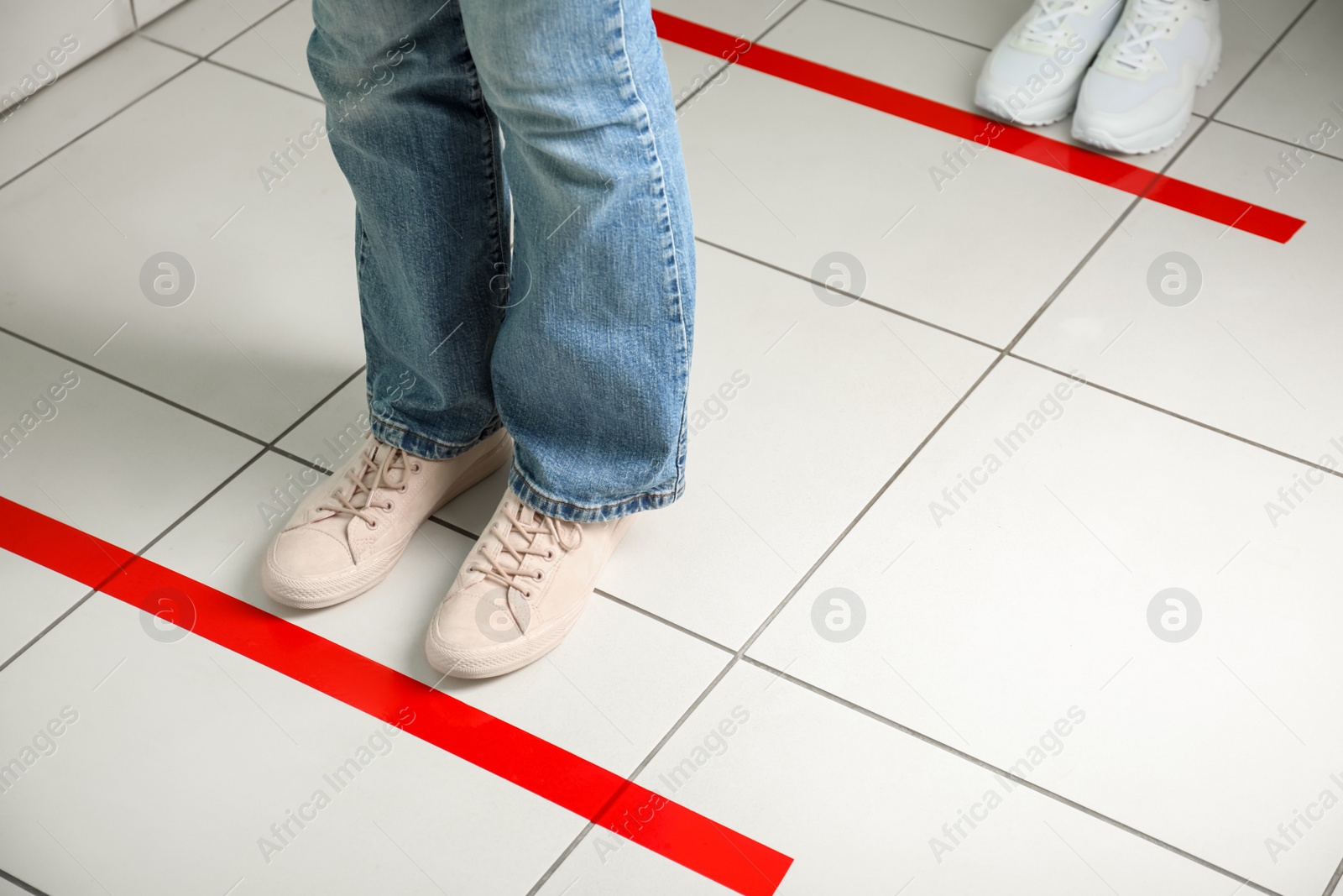 Photo of People standing in line behind taped floor markings for social distance, closeup. Coronavirus pandemic