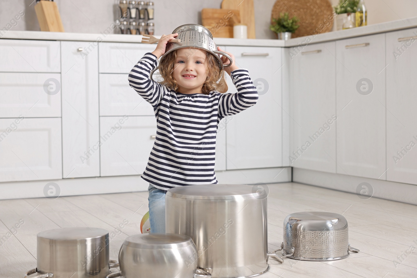 Photo of Little girl pretending to play drums on pots in kitchen