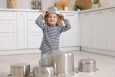 Little girl pretending to play drums on pots in kitchen