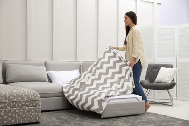 Photo of Woman making sleeping place for guest in living room. Convertible sofa