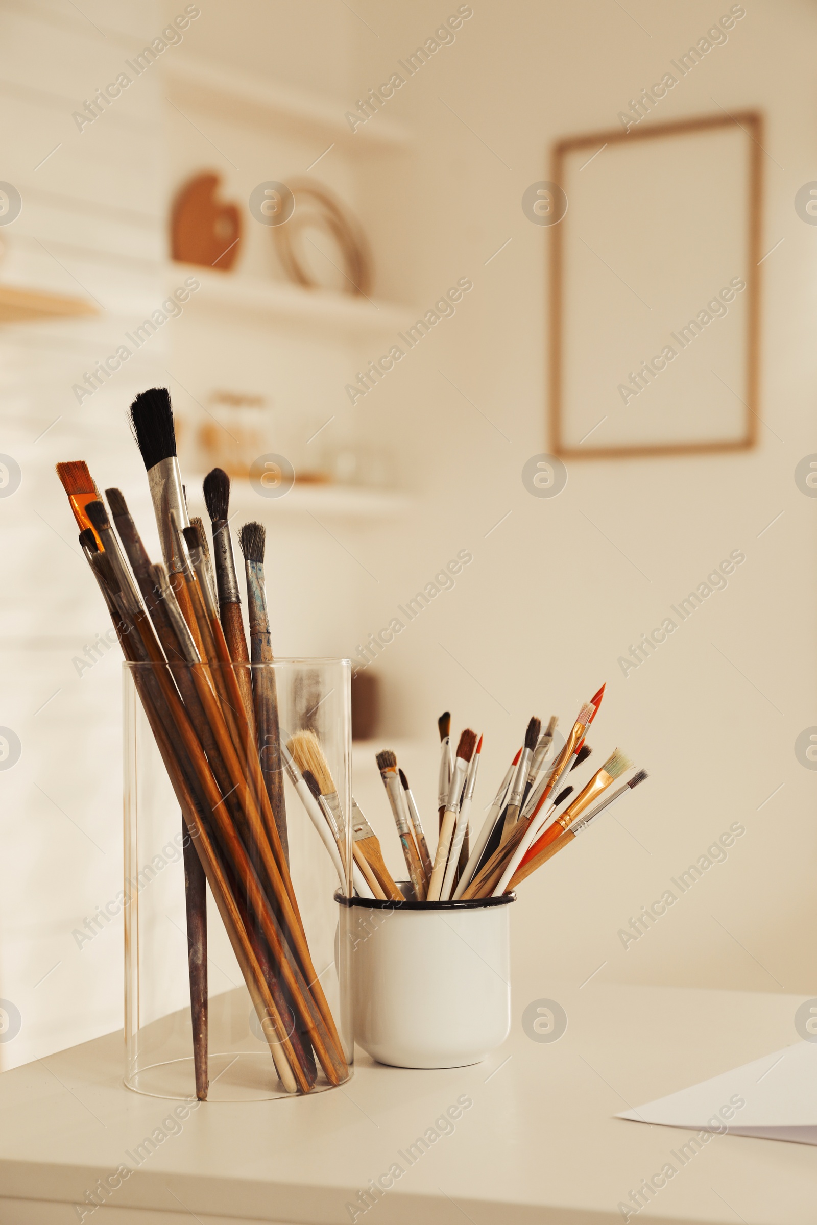 Photo of Holders with different paintbrushes on white table in studio. Artist's workplace