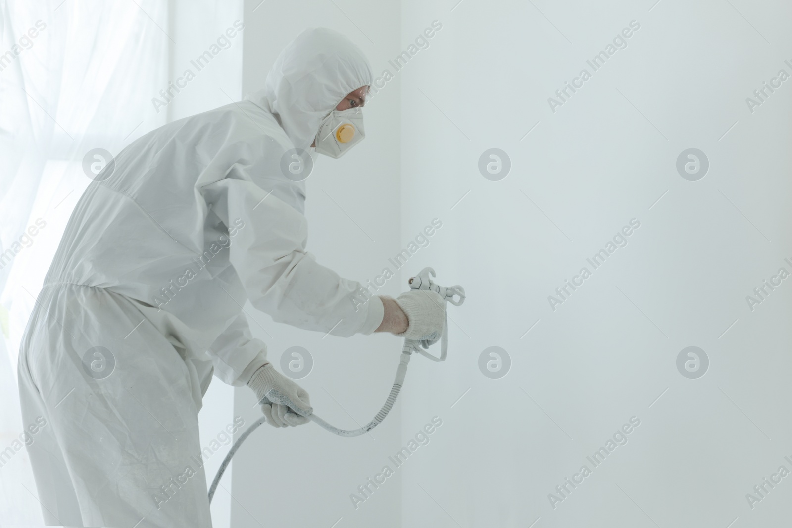 Photo of Decorator painting wall with spray indoors, space for text