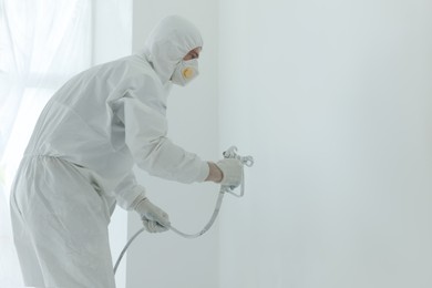 Decorator painting wall with spray indoors, space for text
