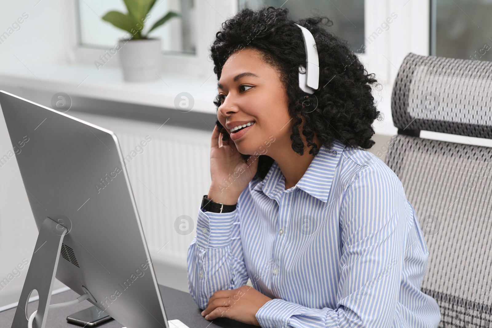 Photo of Young woman with headphones working on computer in office