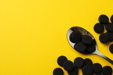 Photo of Activated charcoal pills and spoon on yellow background, flat lay with space for text. Potent sorbent