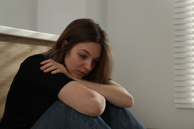 Photo of Sad young woman sitting on indoors, space for text