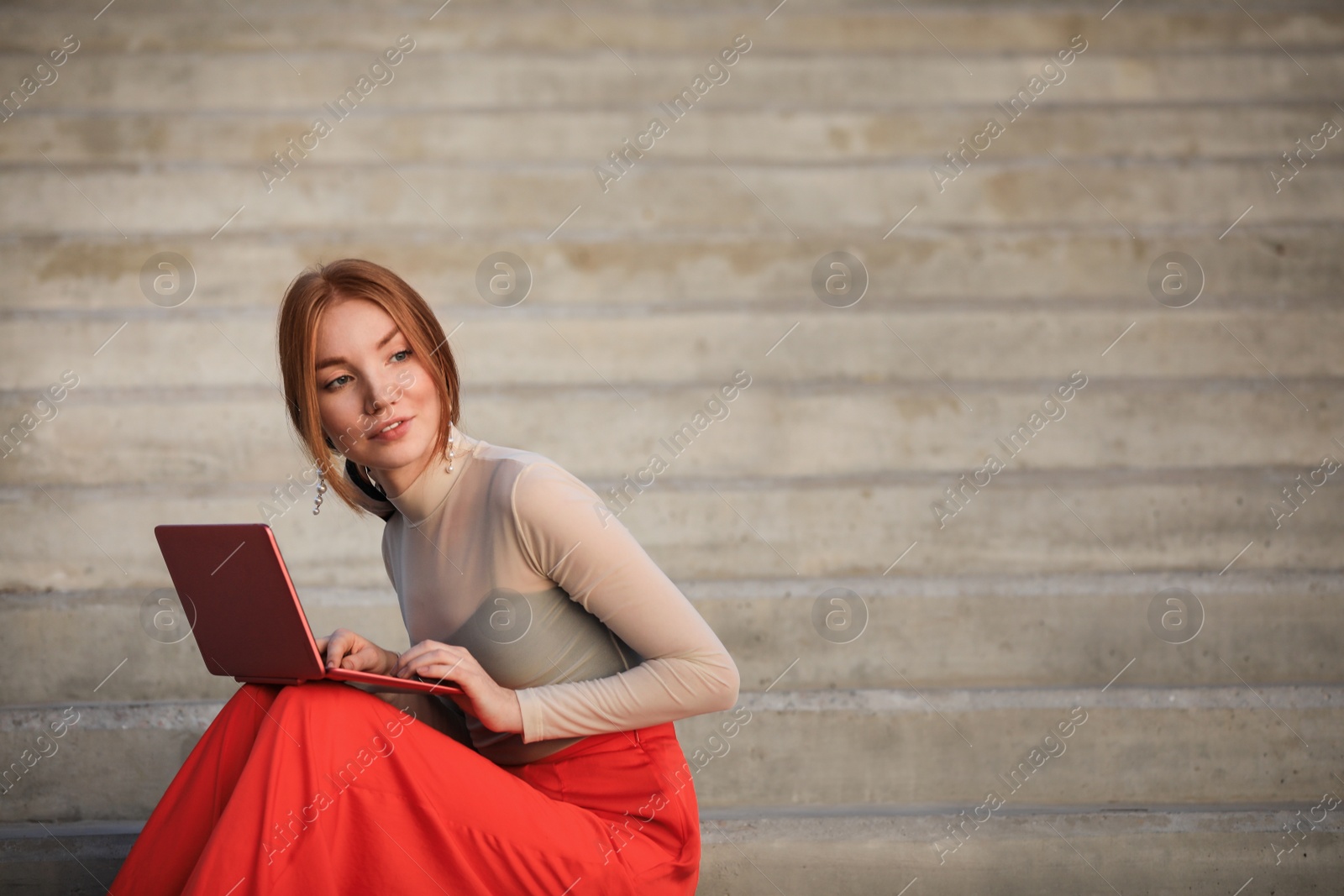 Photo of Beautiful young woman with laptop sitting on stairs outdoors