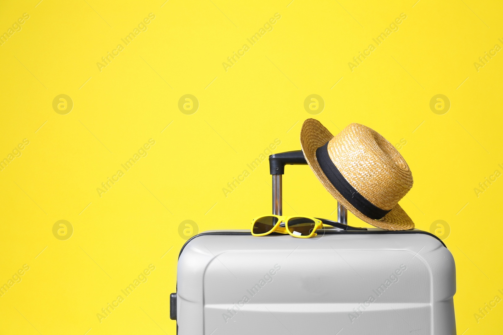 Photo of Stylish grey suitcase with hat and sunglasses on yellow background. Space for text