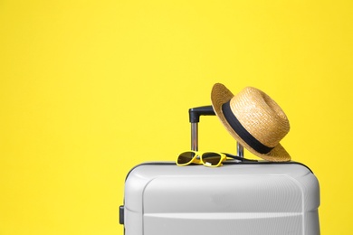 Stylish grey suitcase with hat and sunglasses on yellow background. Space for text